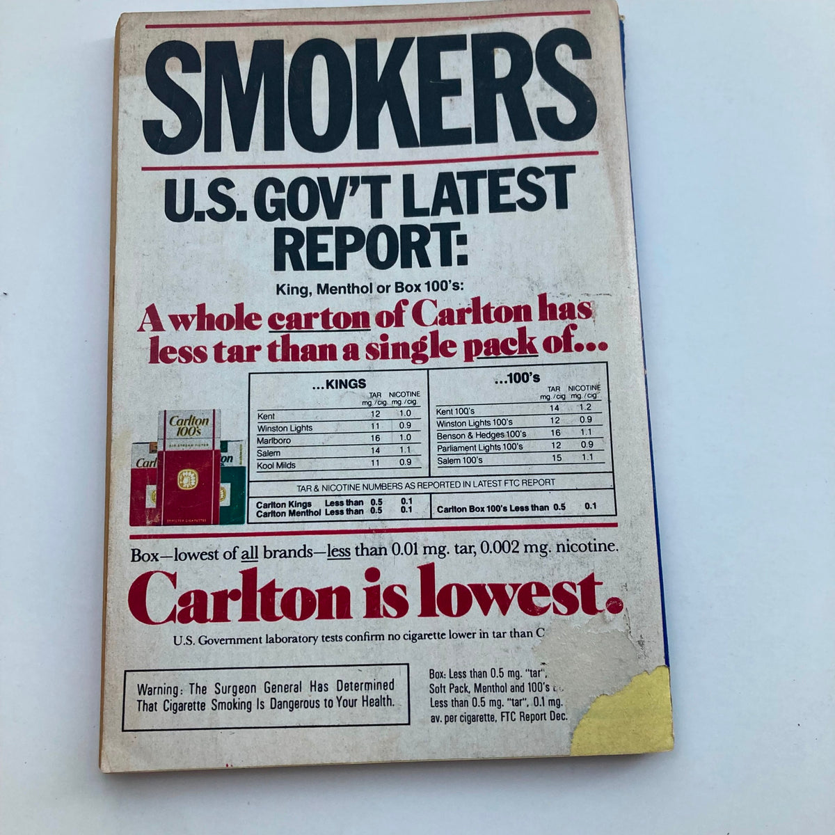 Back cover of a magazine displaying a cigarette advertisement for Carlton, highlighting tar and nicotine levels, with a warning about smoking dangers.