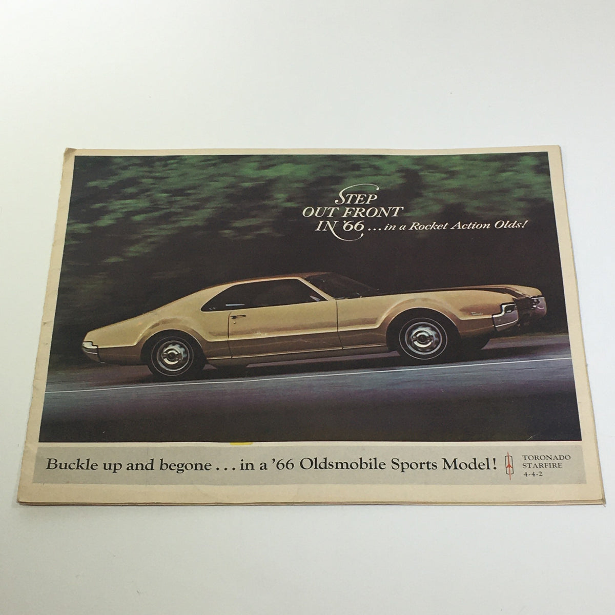 1966 Oldsmobile Sports Model Tornado-Starfire brochure cover featuring a stunning gold car driving on a scenic road, with text urging to 'Step Out Front in a Rocket Action Olds!'.