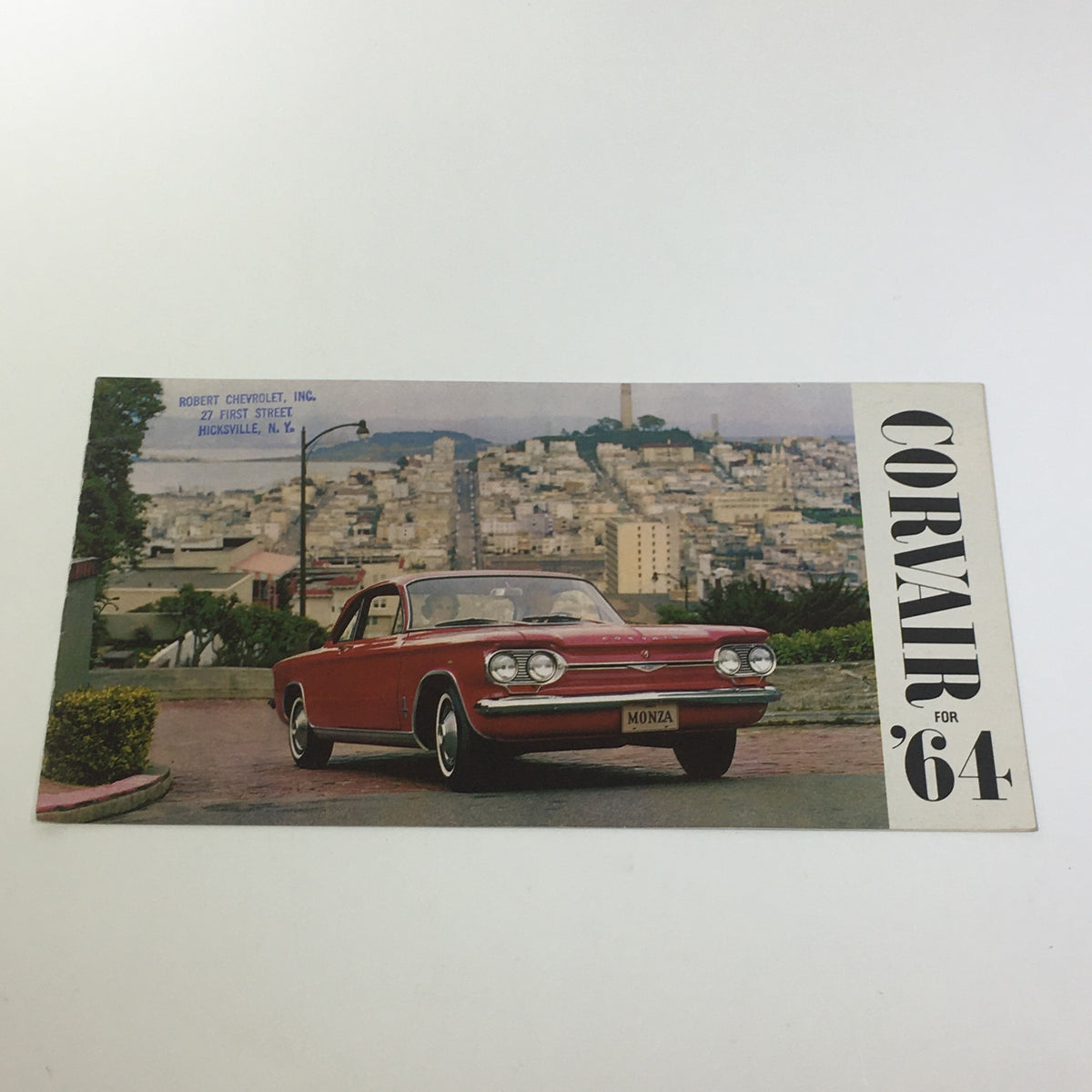 1964 Corvair by Chevrolet Turbo-Supercharged V-8 Engine 3-Speed Tran Car Catalog featuring a classic red Corvair Monza parked on a picturesque street with a city view.