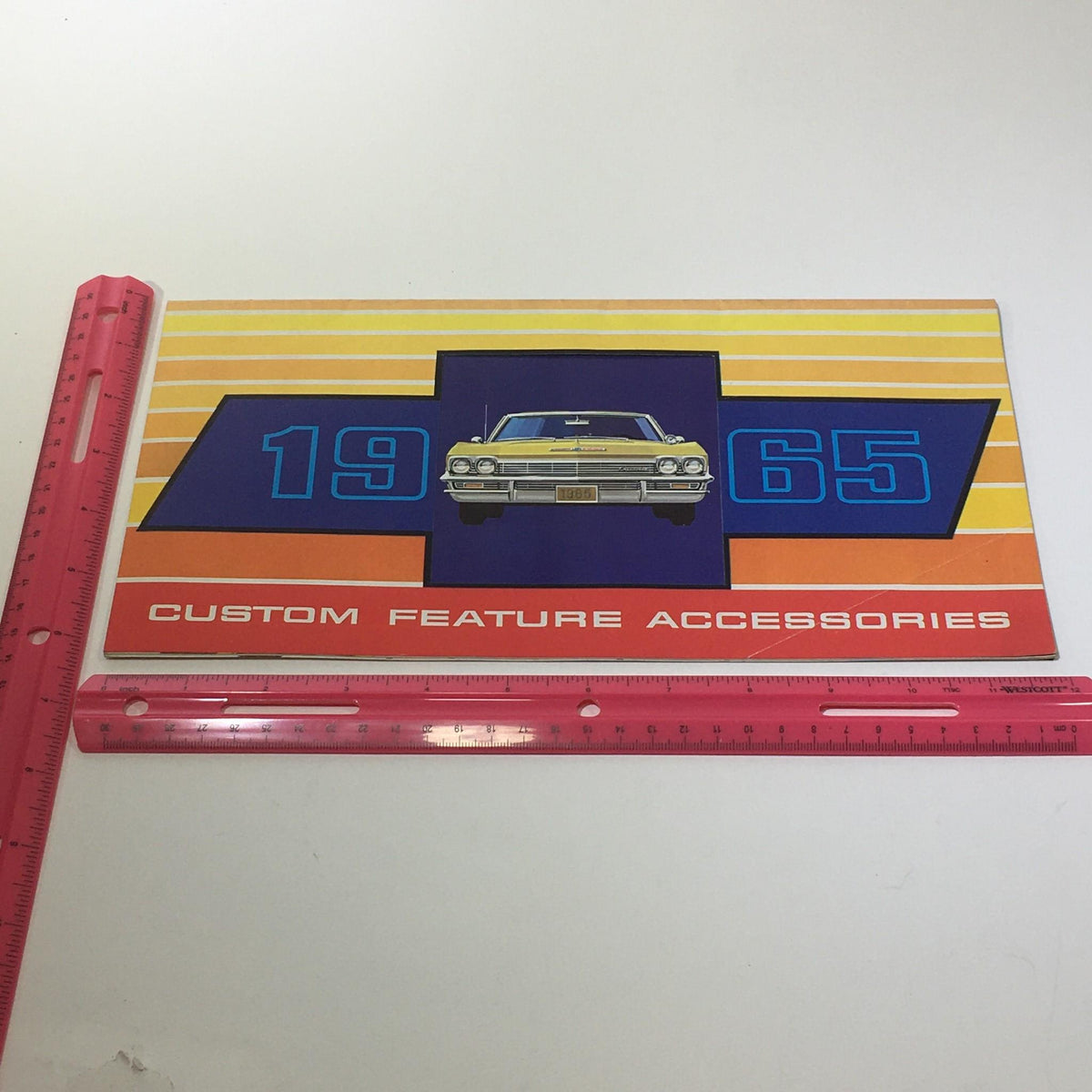Measuring the 1965 Chevrolet Custom Feature Accessories Wire Wheel Cover Car Catalog Brochure with a ruler, to showcase its dimensions.