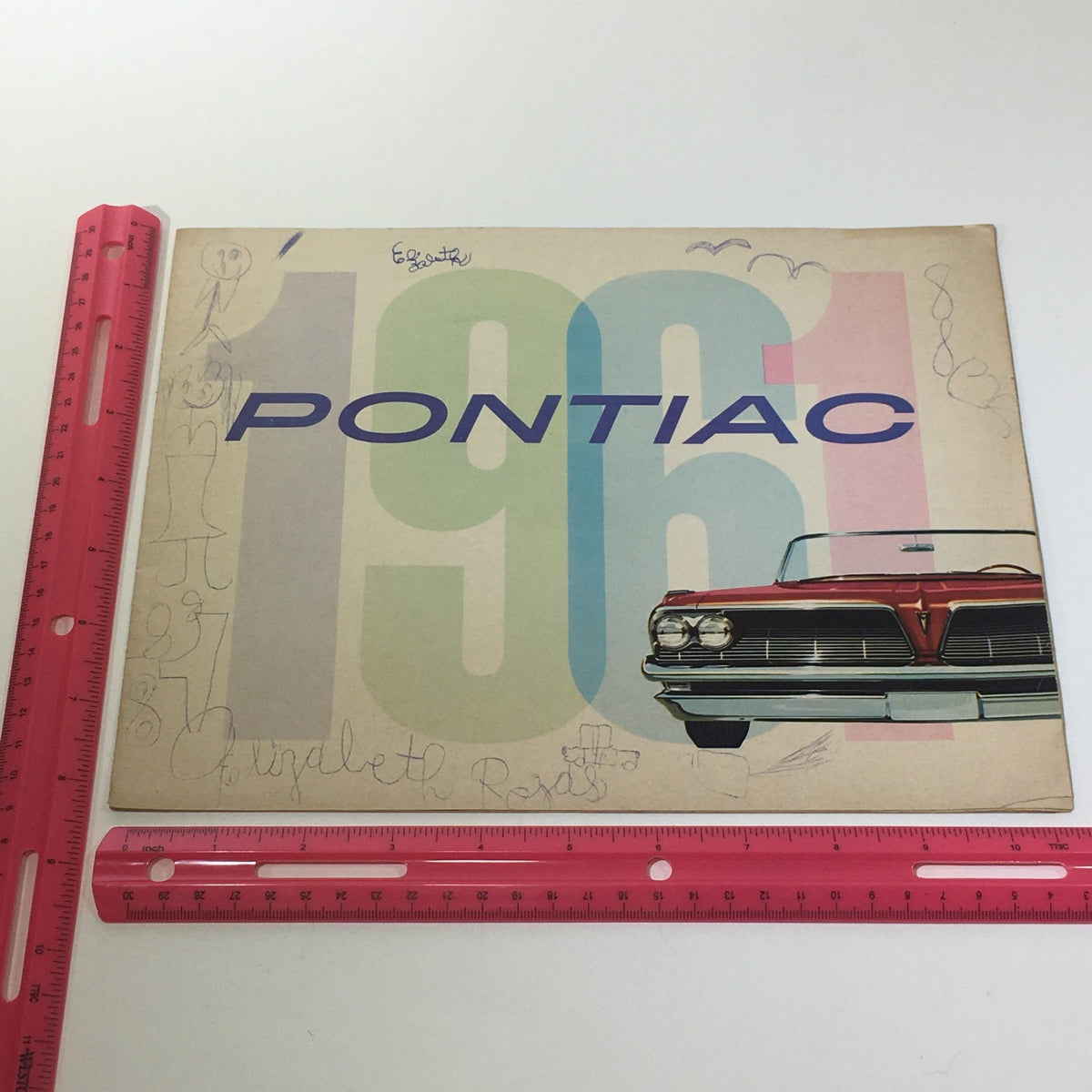 Flat lay of the 1961 Pontiac Catalina Sport catalog with a ruler for size reference, showcasing the vibrant cover design and vintage integrity.