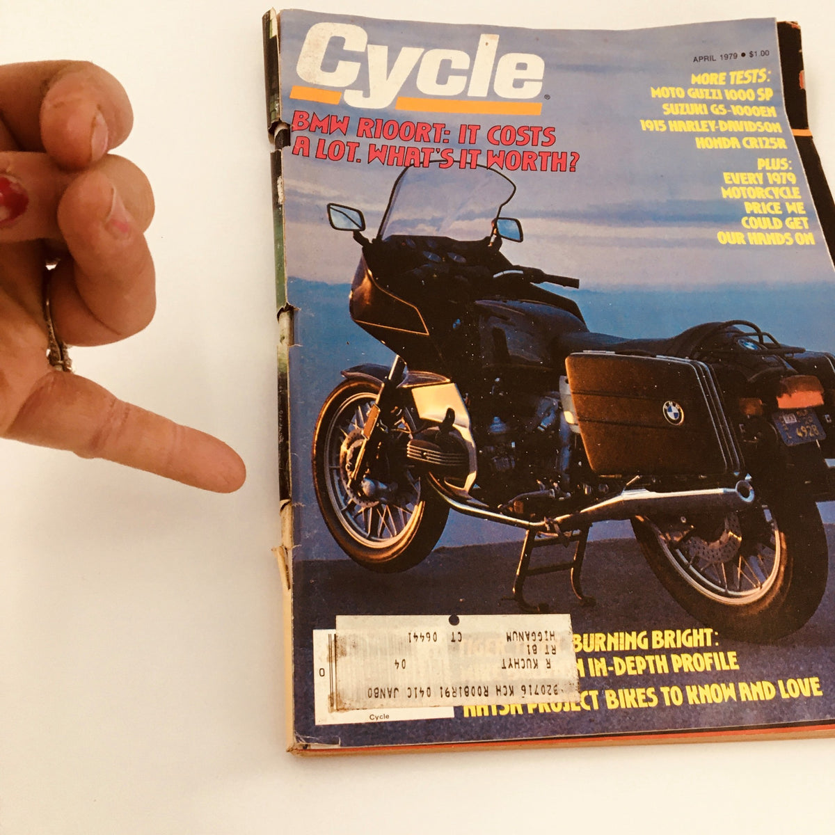 VTG Cycle Magazine April 1979 cover image showcasing the BMW R100RT, emphasizing its features and motorcycle tests, with a hand pointing at the magazine for emphasis.