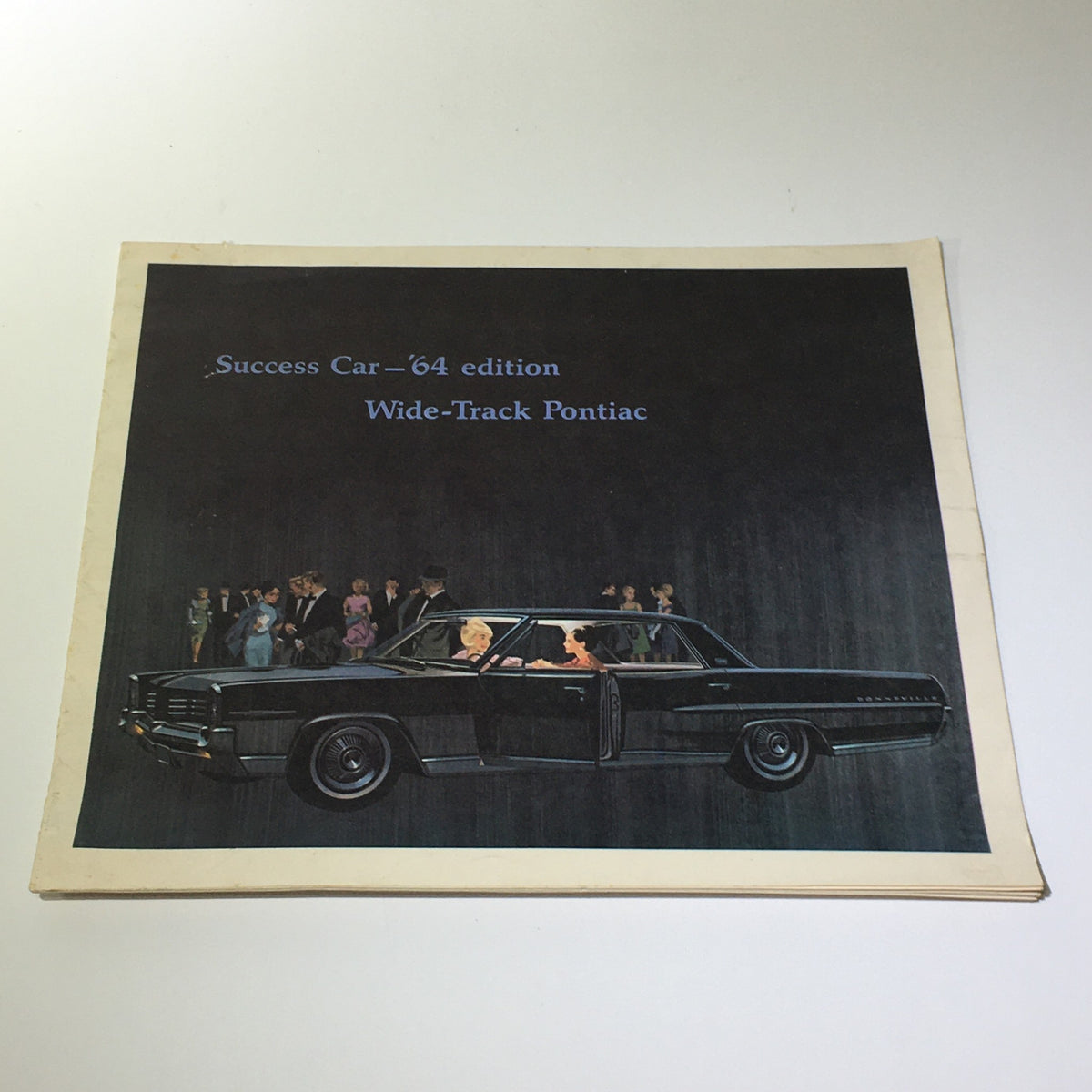 Cover of the 1964 Success Car Edition: Wide-Track Pontiac Trophy V-8 E Car Catalog Brochure featuring a depiction of a black Pontiac car and elegant figures in the background.