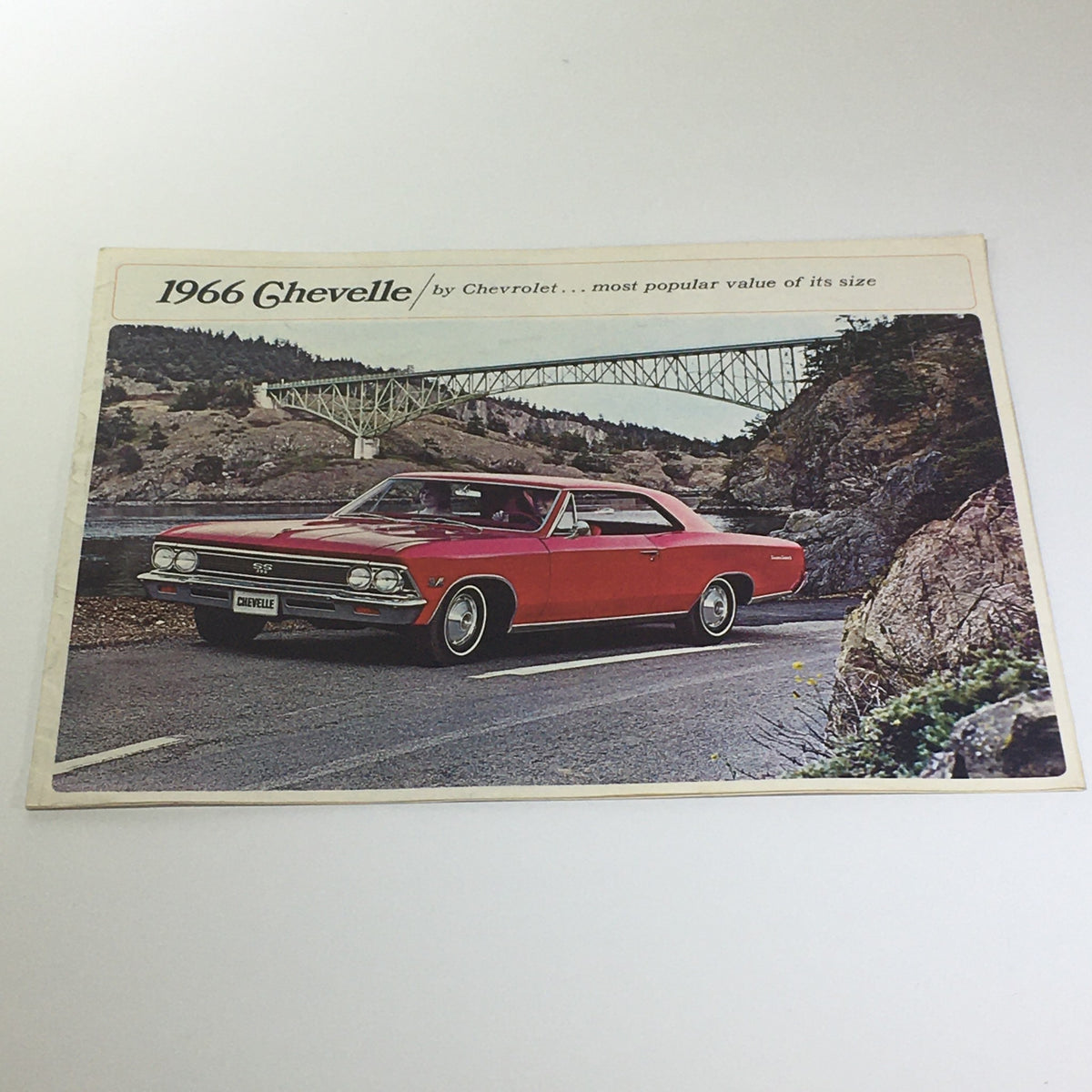 1966 Chevelle 300 Deluxe 2-Door Sedan by Chevrolet on a scenic road, showcasing its classic design and red exterior.