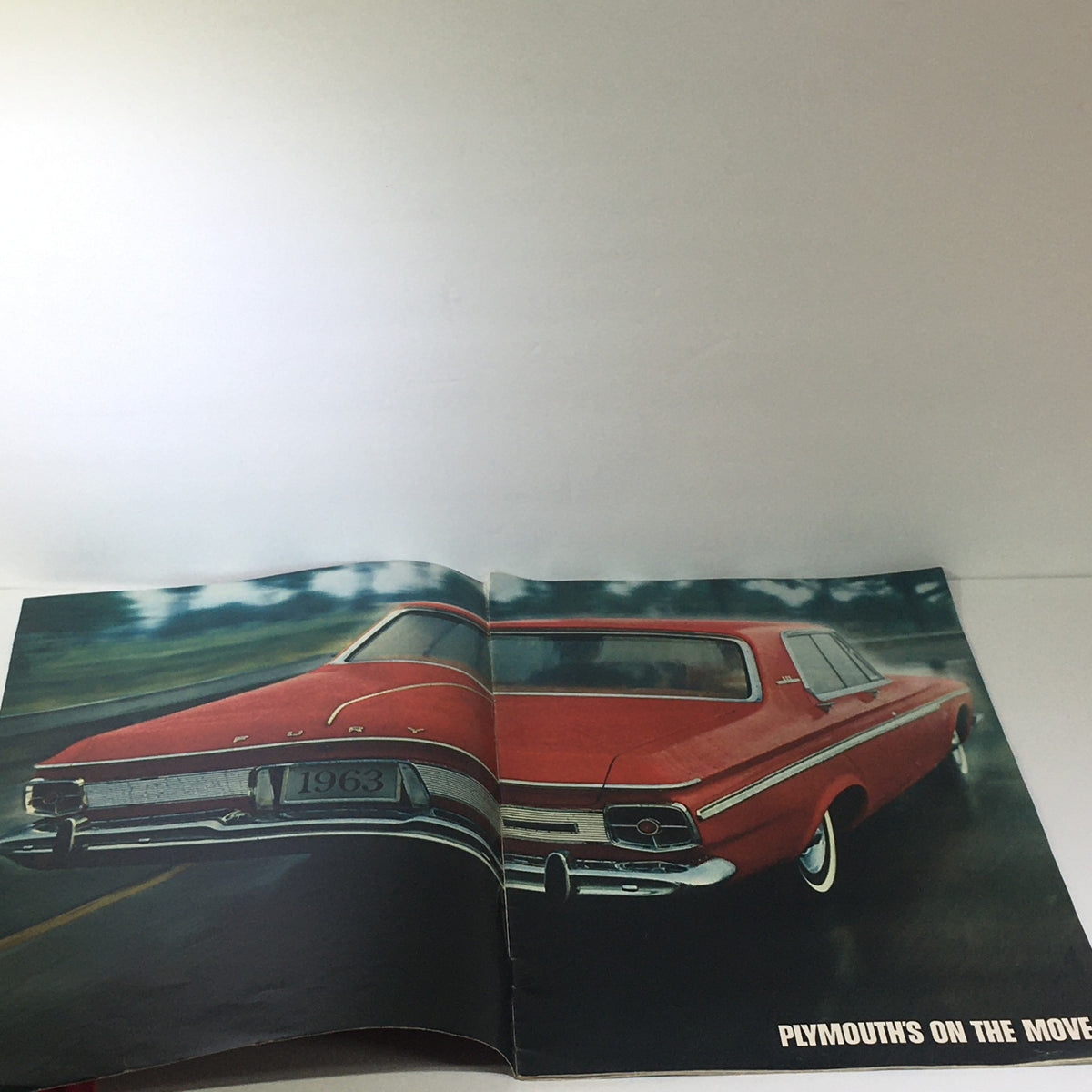 Inside view of the 1963 Plymouth by Chrysler Corp. brochure displaying a striking illustration of a red Plymouth Fury moving on the road, promoting the car's design and performance.