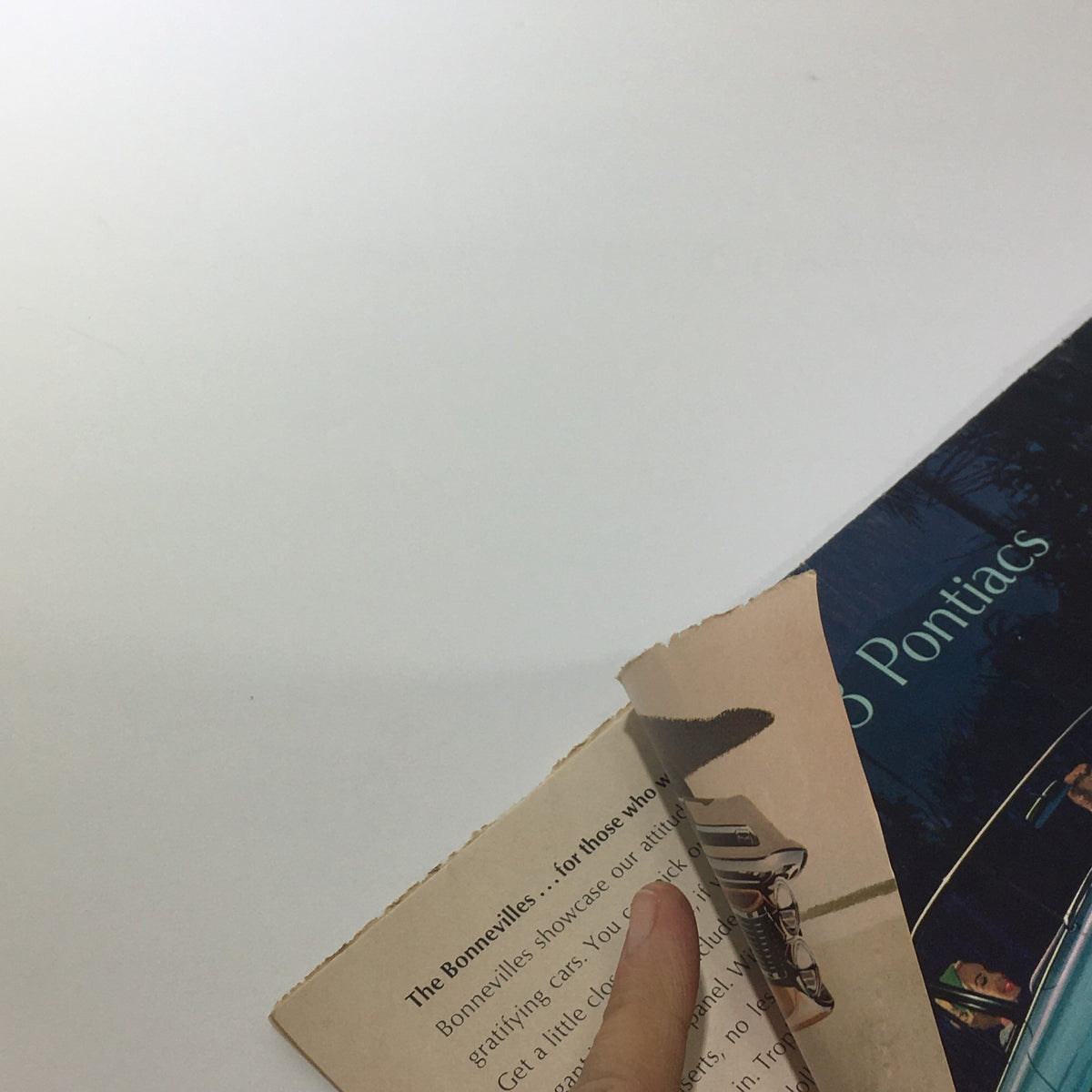Close-up of the damaged edge of the 1963 Pontiacs' The Bonnevilles Convertible 2-Door Sedan Car Catalog Brochure, highlighting its vintage condition.