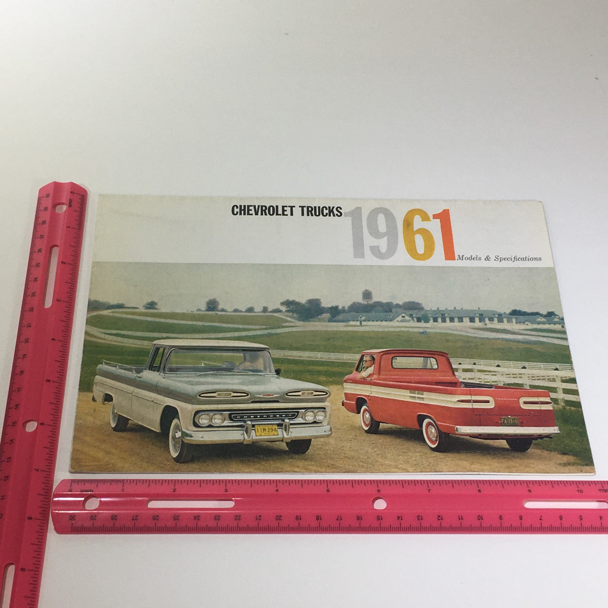 Measuring the cover of Chevrolet Trucks of 1961 Models & Specifications Light-Heavy Duty Trucks Catalog with a ruler, showing the catalog dimensions and design.
