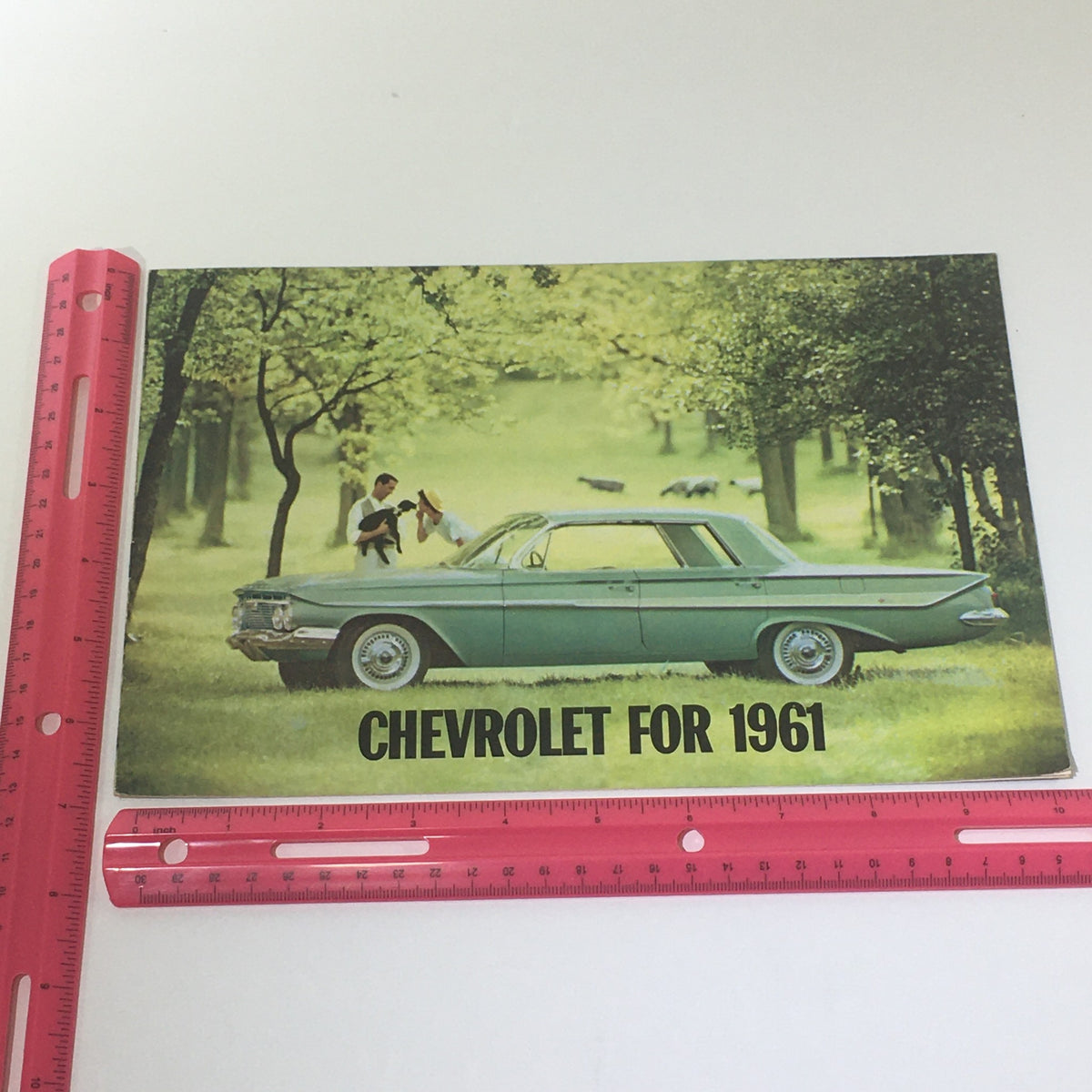 Chevrolet for 1961 Impala Series brochure displayed next to a ruler, highlighting the cover with a green car in a natural setting.