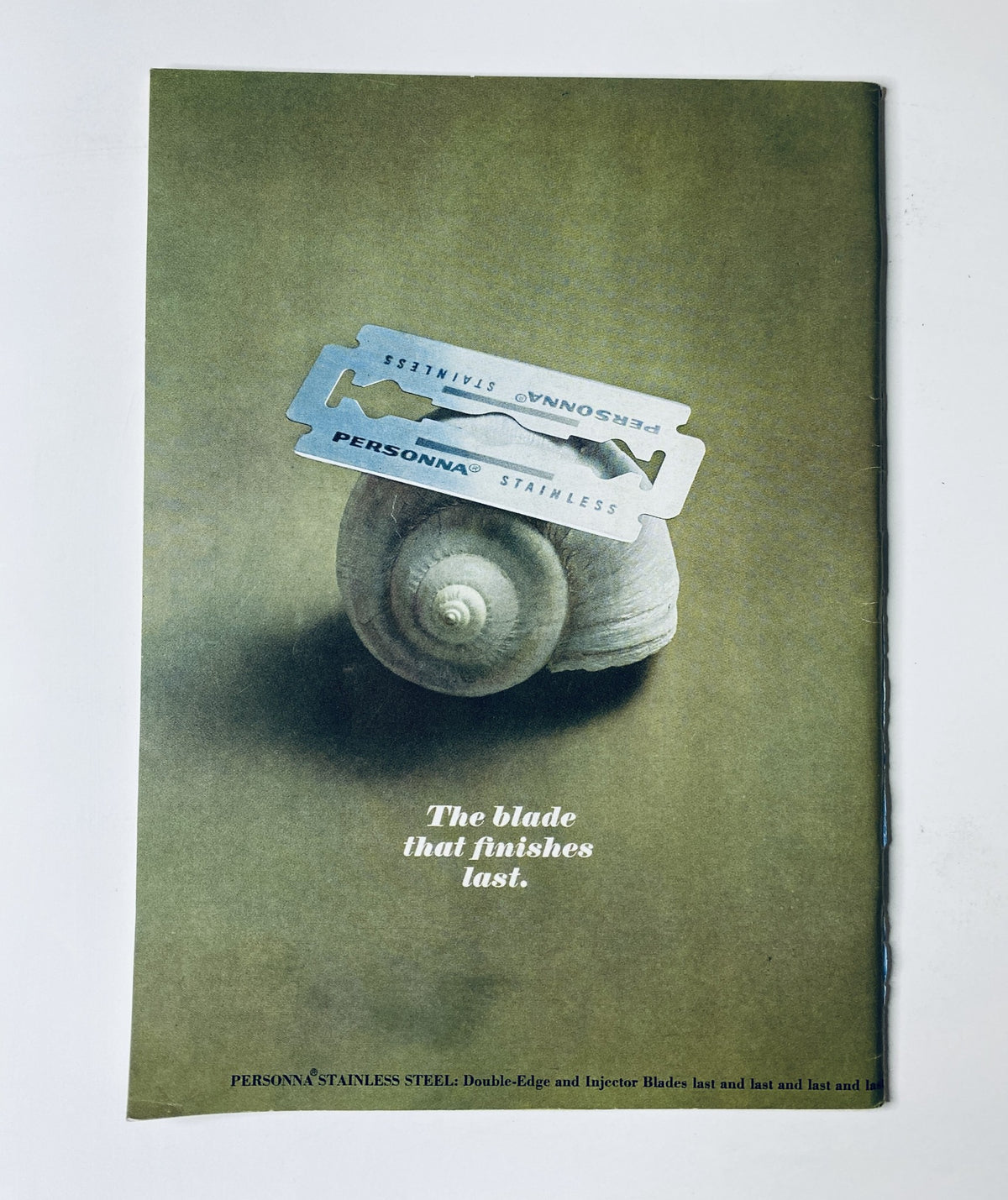Vintage advertisement showcasing a stainless steel double-edge razor blade atop a seashell, conveying the tagline 'The blade that finishes last.' Reflected design elements are emphasized, aligning with 'The New Yorker Magazine July 10, 1965 Swimming Pool Figures Cover A. François VG'.