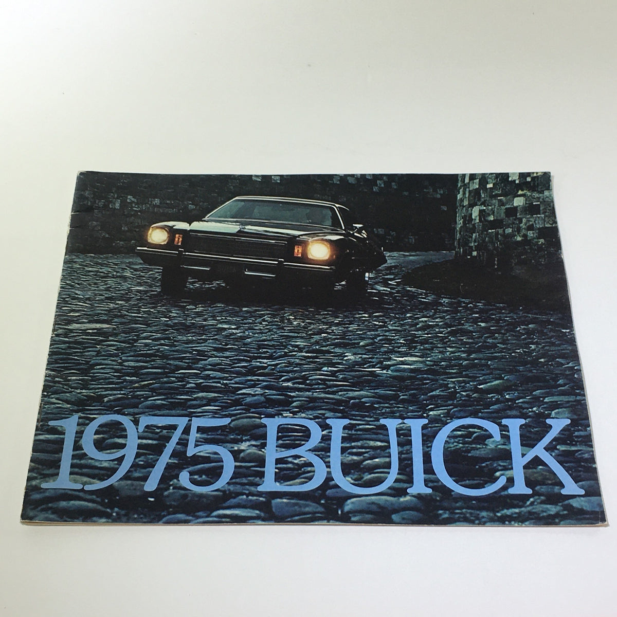 Cover of the Vintage 1975 Buick Skyhawk-Century-Le Sabre-Riviera Hardtop Coupe Car Catalog featuring a classic Buick car on a cobblestone street.