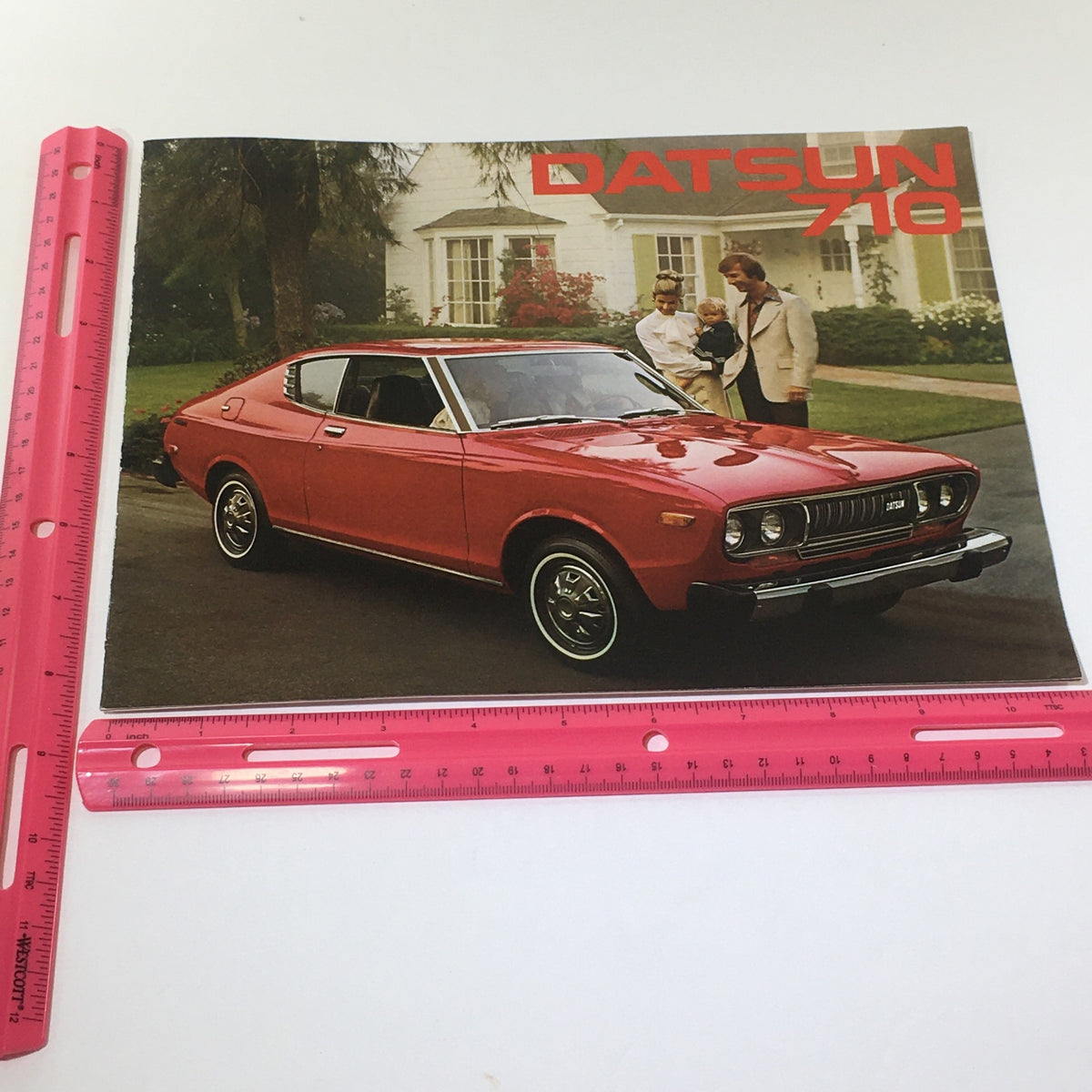 Vintage 1976 Datsun 710 2-Door Hardtop Sedan 100-HP 4-Speed Manual Car Brochure featuring a striking red Datsun 710 parked in front of a stylish home, showcasing its classic design and charm.