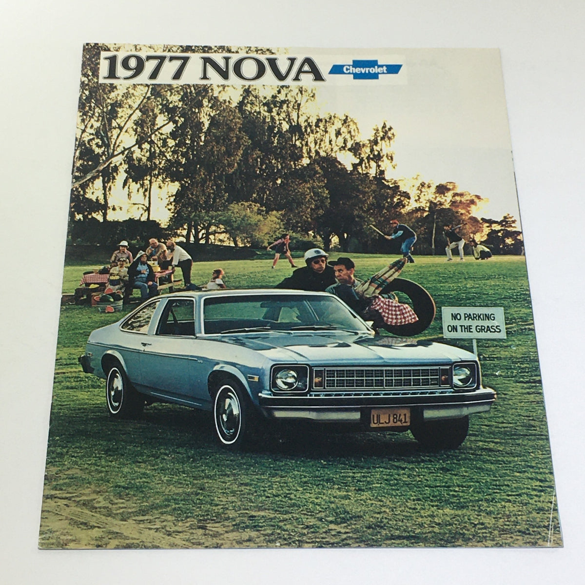 Vintage 1977 Nova Chevrolet 4-Door Hardtop 350-4 V-8 Engine Car Catalog Brochure featuring a blue 1977 Nova with people enjoying a day at the park.