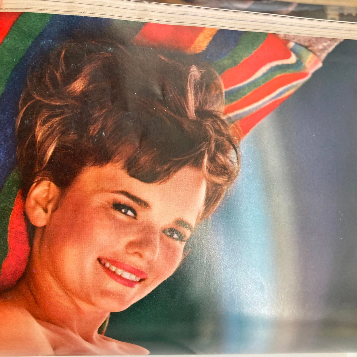 Centerfold image from VTG Playboy Magazine June 1966 showcasing a woman with short hair, smiling while lounging on colorful striped fabric.