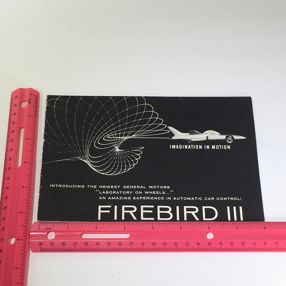 An image of the Vintage The New Firebird III - Fire I & II Electro-Hydraulic Control Car Catalog next to a ruler, illustrating its size and design.
