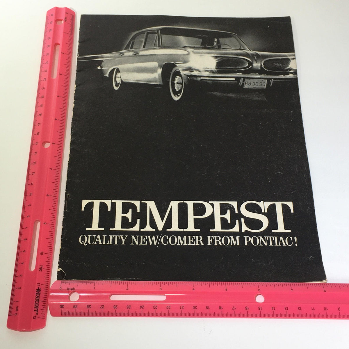 Vintage Pontiac Tempest catalog brochure cover with a ruler showing dimensions, featuring the phrase 'QUALITY NEW/COMER FROM PONTIAC' and an image of a classic car.