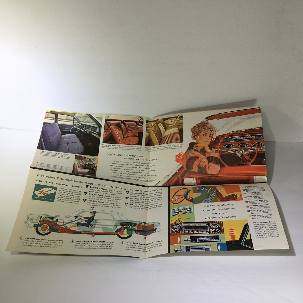 Interior pages of the Vintage 1961 Oldsmobile 2-Door Hardtop Sedan Twin-Triangle Stability Car Catalog displaying illustrations of car interiors and engineering features, highlighting the innovative design.