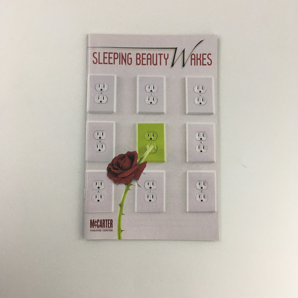 Cover of the 2011 McCarter Theatre Center 'Sleeping Beauty Wakes' featuring a design with electrical outlets and a rose.