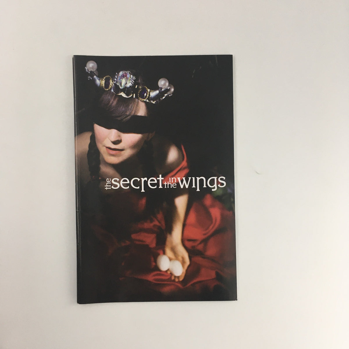 Cover of 'The Secret in the Wings' by Mary Zimmerman, featuring a figure in a red dress and a crown, showcasing the artistic theme of the McCarter Theatre Center production from 2005.