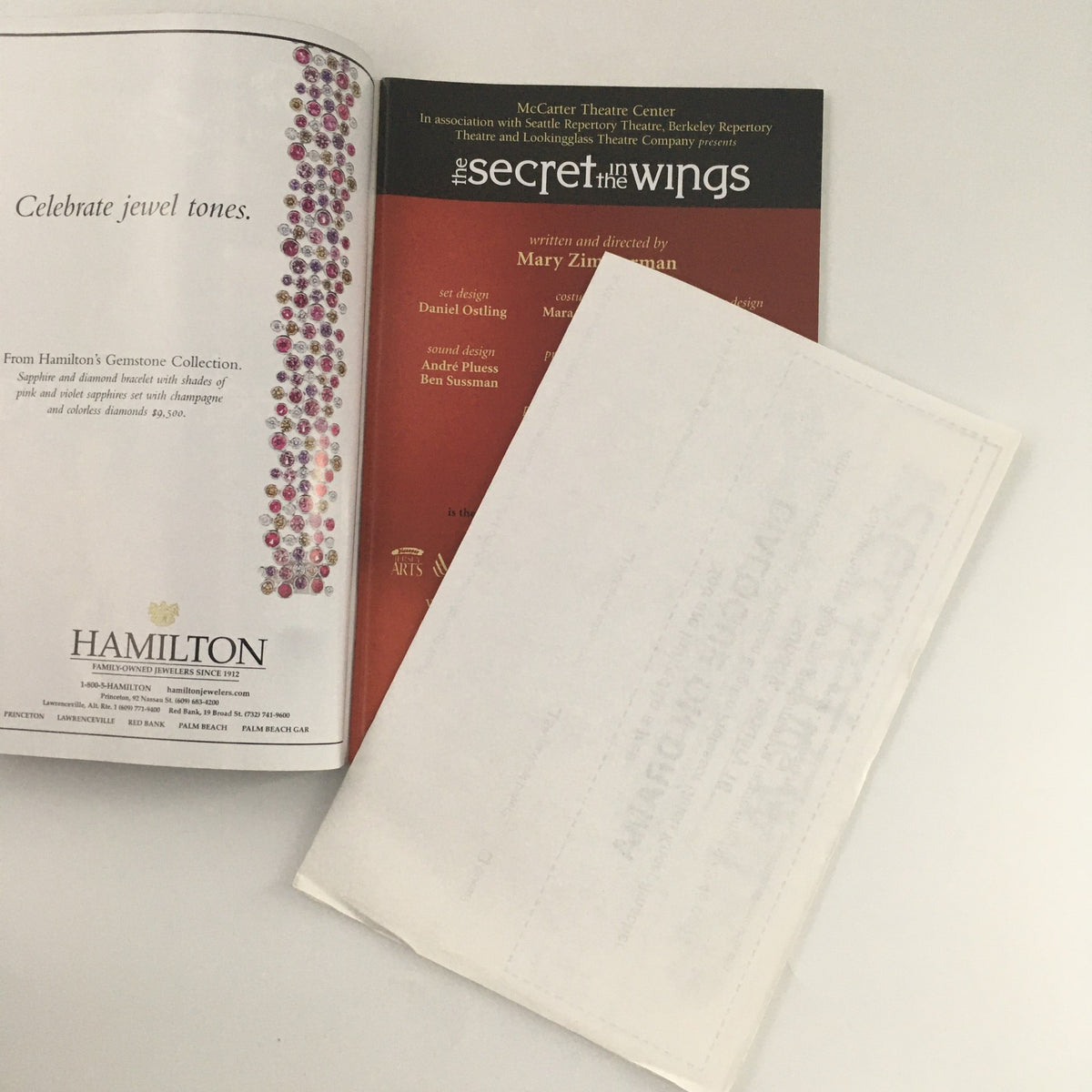 2005 McCarter Theatre Center program for 'The Secret in the Wings' written by Mary Zimmerman, featuring information about the production and details about the cast and crew, presented alongside a protective plastic cover.