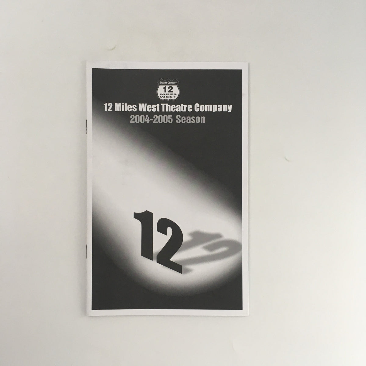 Cover of the 2004-2005 season program for 12 Miles West Theatre Company featuring the number 12, promoting the production 'Tea for Three Lady Bird, Pat & Betty'.
