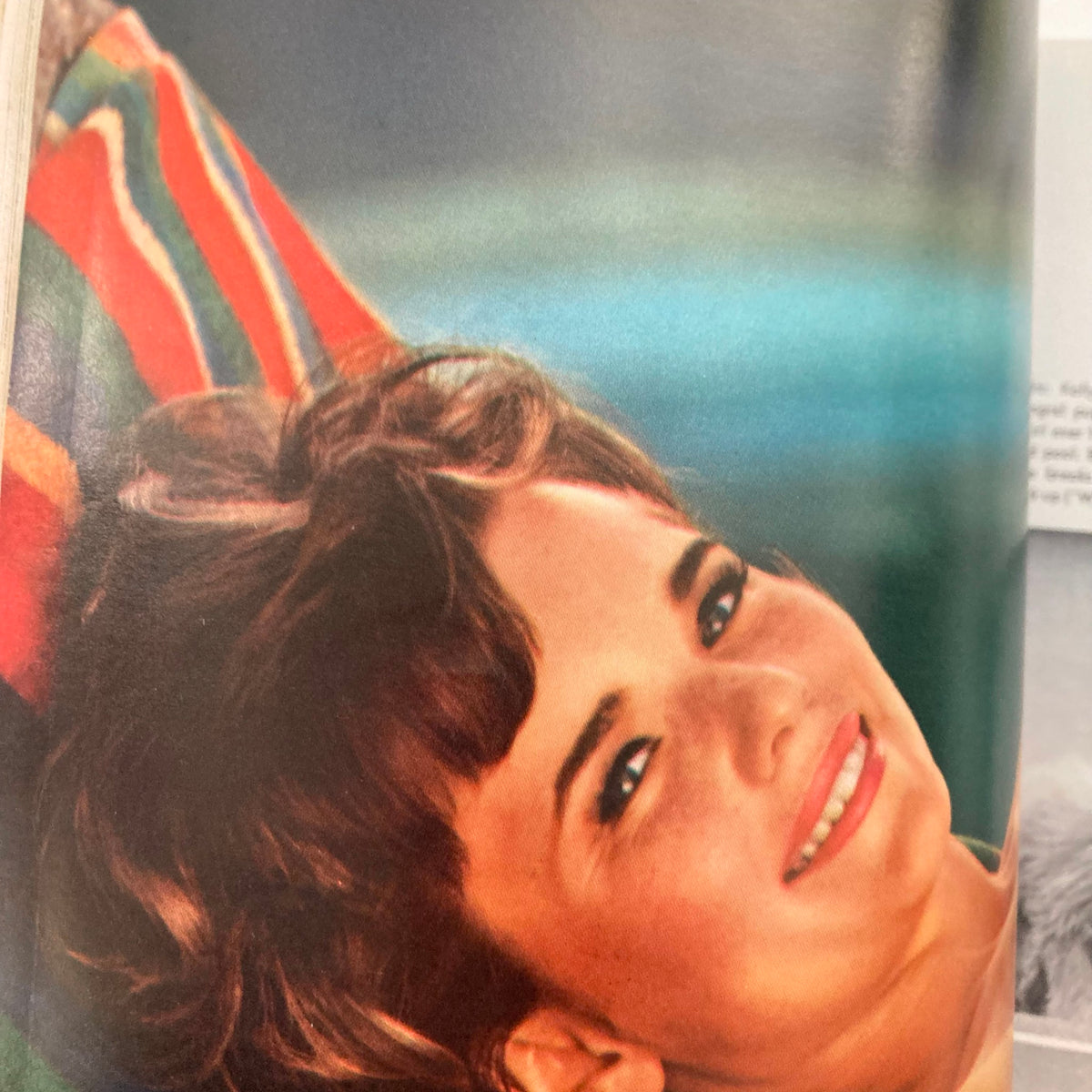 Playmate Kelly Burke from the June 1966 VTG Playboy Magazine, lying on a colorful striped blanket with a bright smile.