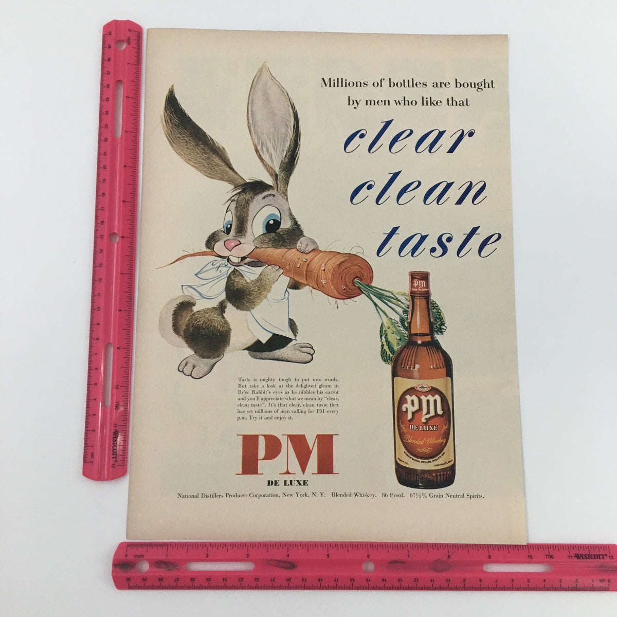 1950 PM De Luxe Blended Whiskey 86 Proof Vintage Print Ad, featuring a cartoon bunny with a ruler for scale, promoting clear clean taste.