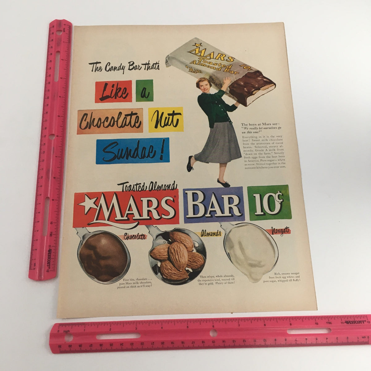 Mars Toasted Almond Bar Vintage Print Ad emphasizing the candy's features with a woman cheerfully holding a Mars Bar, with text explaining the flavors and ingredients including chocolate, almonds, and nougat.