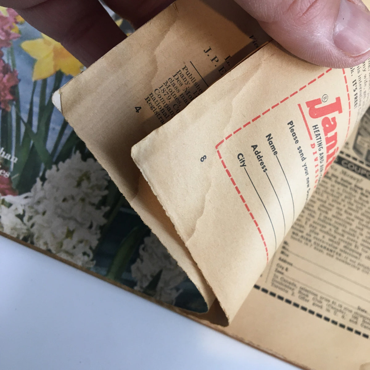 Close-up of inside pages of Better Homes & Gardens Magazine January 1956 with an advertisement page and a hint of floral illustrations.