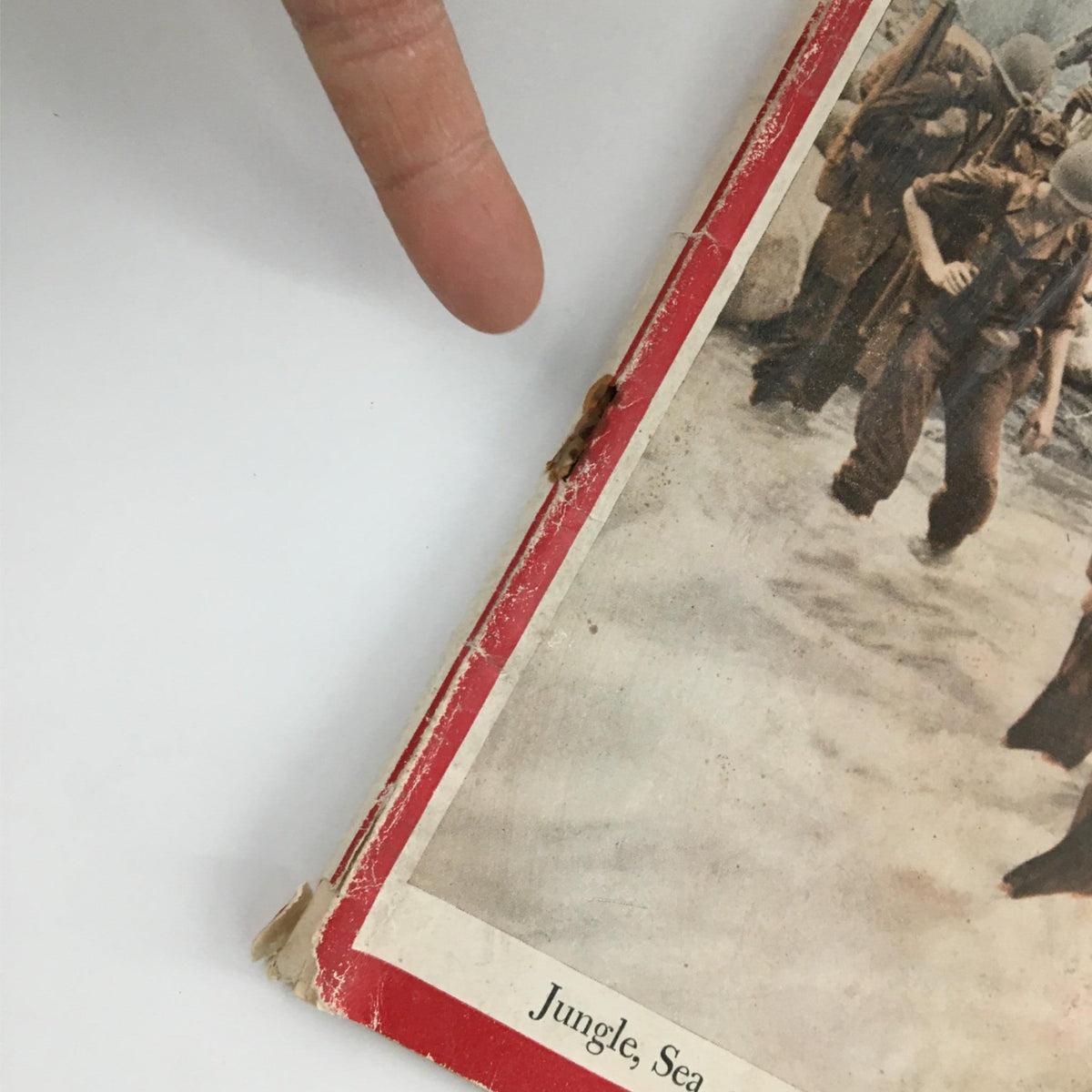 Close-up of the damaged spine of Newsweek Magazine January 18, 1943, showcasing wear and tear, with a finger pointing to the frayed area. The magazine features the title "Jungle, Sea, or Air, Three-Dimensional War" highlighting its historical significance.