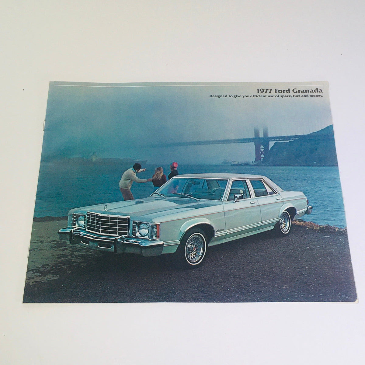 1977 Ford Granada sales brochure cover featuring a light blue Ford Granada with a scenic backdrop of a bridge, showcasing the car's design and ambiance.