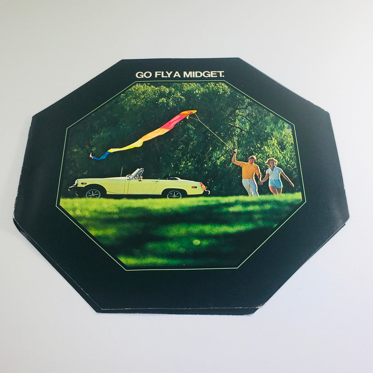 1977 MG Midget Octagon Go Fly A Midget Auto Car Sales Catalog Brochure cover featuring a yellow MG Midget sports car and two people flying a colorful kite in a green field.