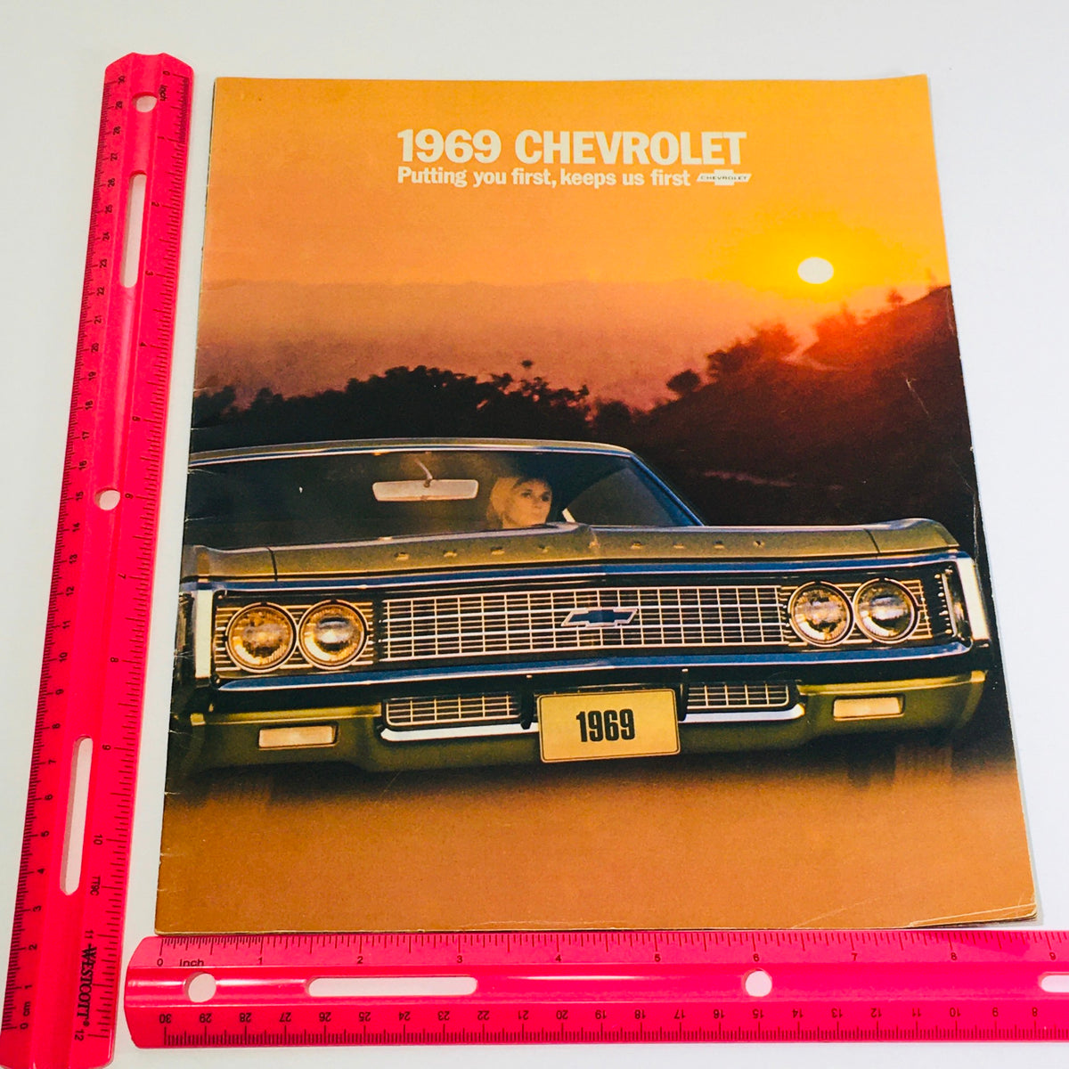 1969 Chevrolet Caprice Dealership Car Auto Brochure Catalog displaying the front view of a green Caprice with a striking grille, set against a sunset backdrop, emphasizing its classic design.