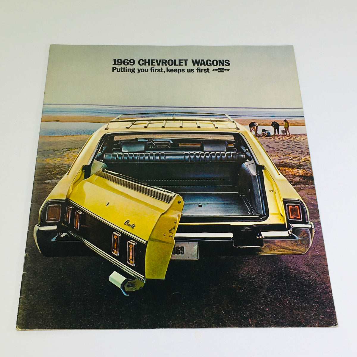 1969 Chevrolet Kingswood Estate Wagons Dealership Car Auto Brochure Catalog featuring a vibrant yellow Chevrolet wagon parked on a beach with the rear door open, showcasing the spacious interior and nostalgic design.