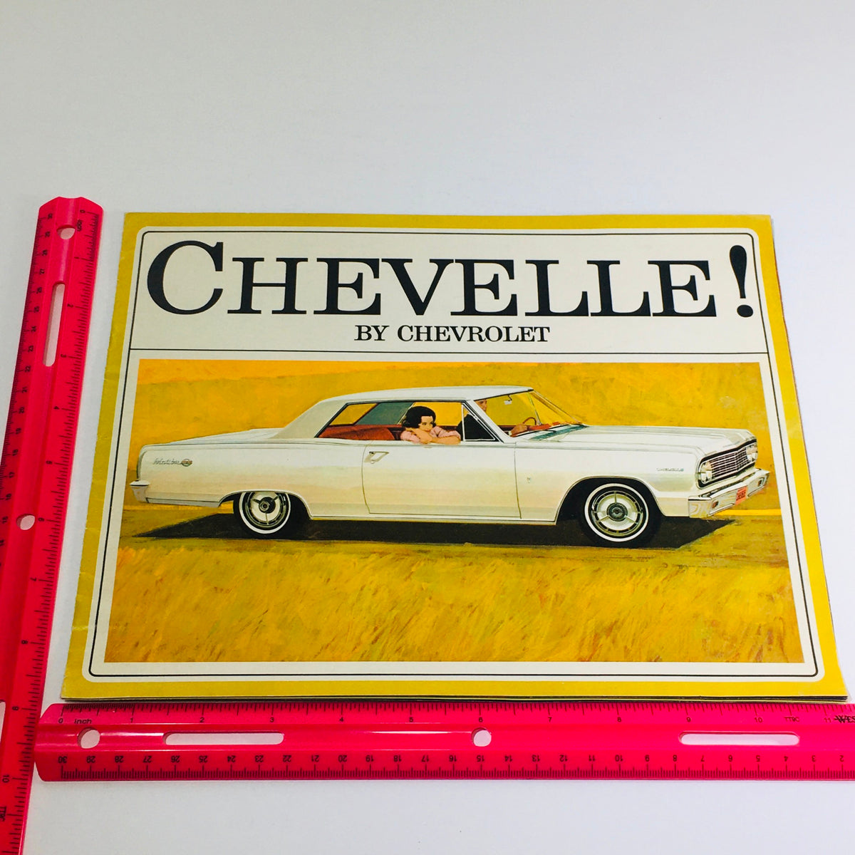 Close-up of the cover of the 1964 Chevrolet Chevelle Malibu Brochure with a ruler for scale, showing its vintage design.