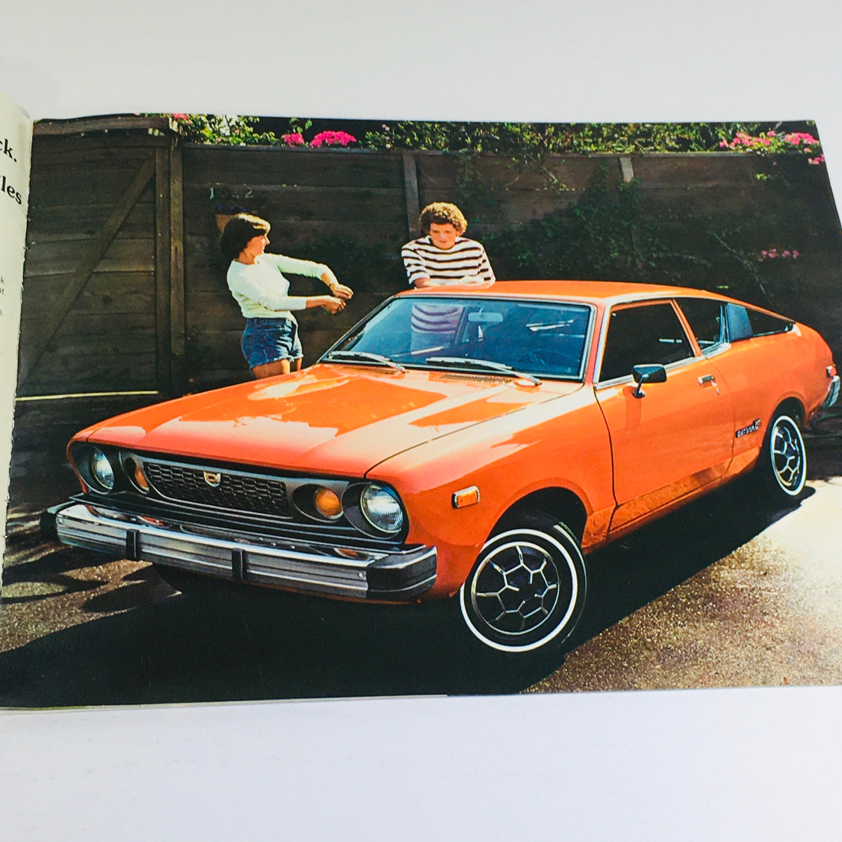 1975 Datsun B-210 Specifications Dealership Car Auto Brochure Catalog featuring an orange Datsun B-210 with two individuals discussing it in a vibrant garden.