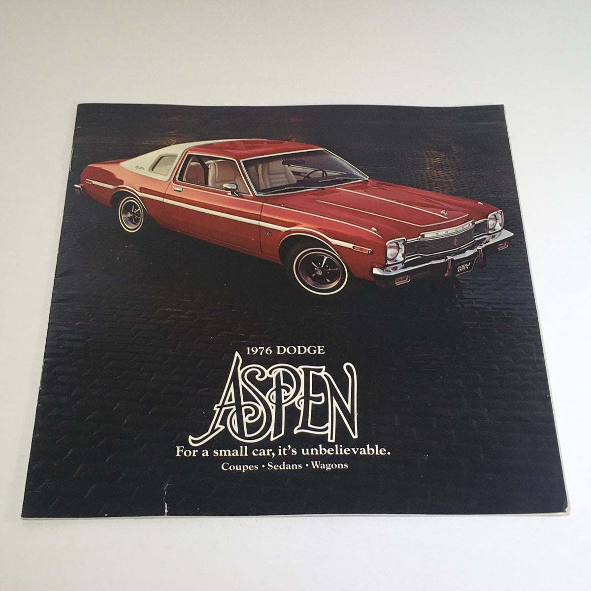 1976 Dodge Aspen Coupe, showing the front view of the car on a textured background. Dealership car auto brochure catalog.