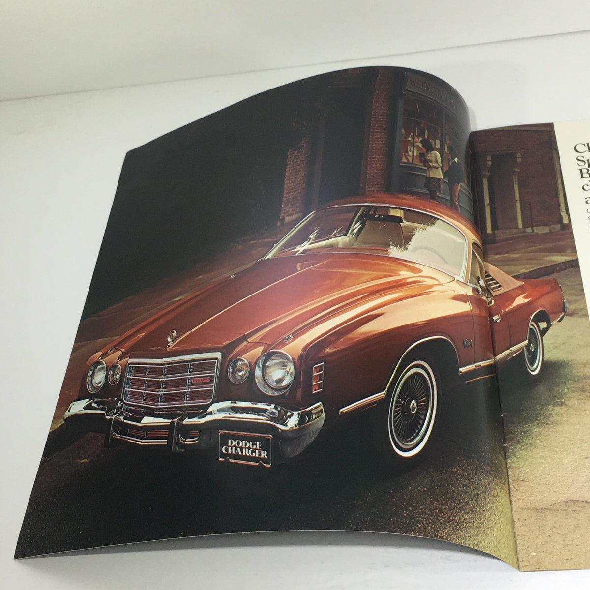 Interior page of the 1976 Dodge Charger brochure presenting a side view of an orange Dodge Charger parked in a vintage setting, highlighting its elegant features.