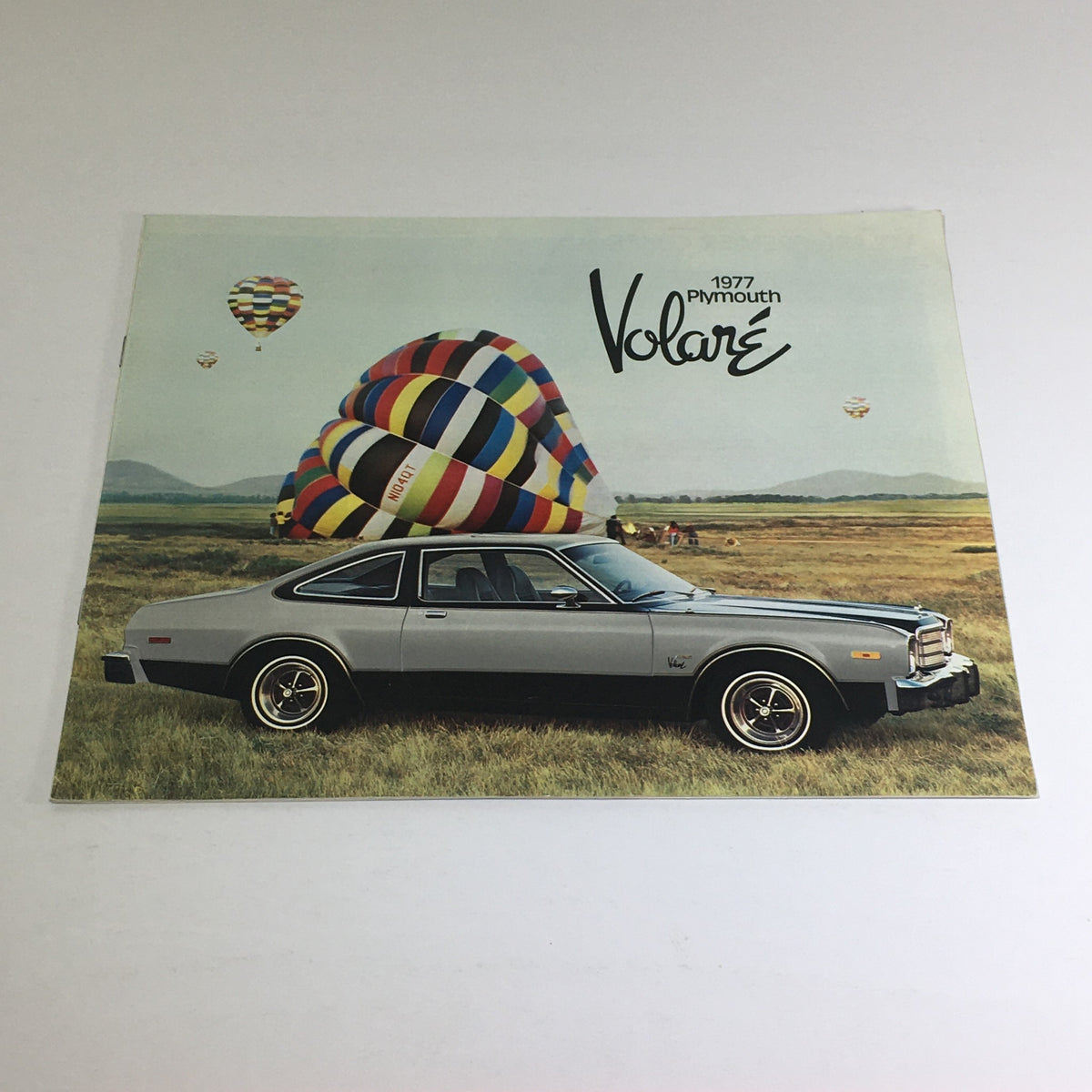 1977 Plymouth Volare Custom Two-Tone Coupe showcased in an outdoor setting with colorful hot air balloons in the background, featured in a vintage dealership car auto brochure catalog.
