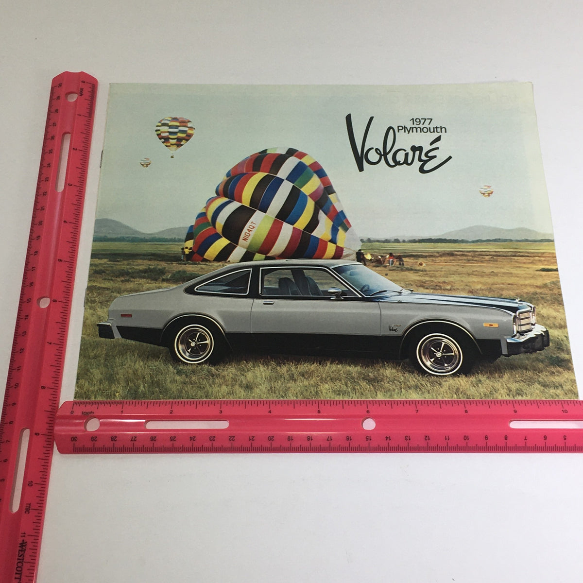 Front cover of the 1977 Plymouth Volare Custom Two-Tone Coupe brochure featuring a silver car next to a colorful hot air balloon in a scenic outdoor setting.