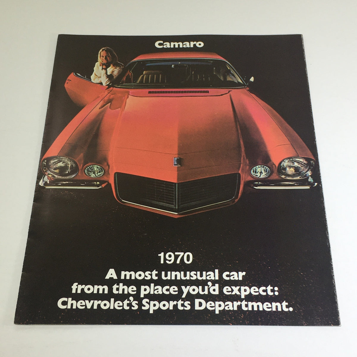 1970 Chevrolet Camaro Sport Coupe Z-25 Dealership Car Auto Brochure Catalog featuring a vibrant red Camaro with a woman posing beside it. The brochure highlights the unique features of this classic car model, with an advertisement stating 'A most unusual car from the place you'd expect: Chevrolet's Sports Department'.