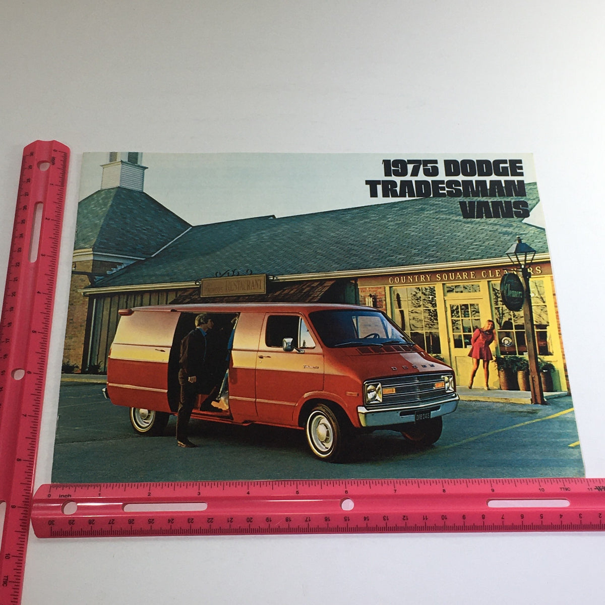 1975 Dodge Trucks Tradesman Vans Dealership Car Auto Brochure Catalog with a ruler for size reference, showcasing an orange Dodge Tradesman van.