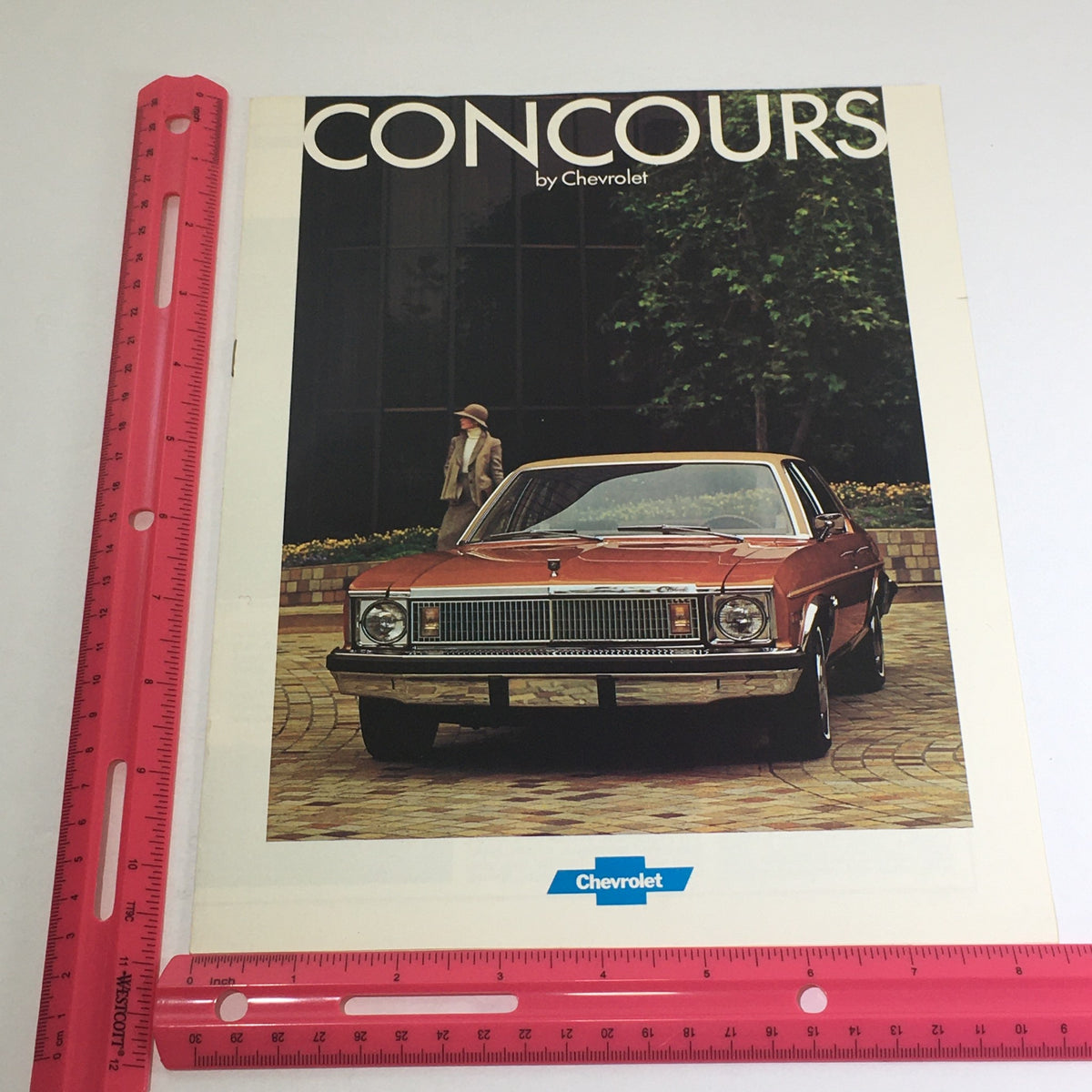 1977 Concours by Chevrolet specifications dealership car auto brochure catalog showcasing a classic Chevrolet vehicle in an outdoor setting, with a woman in vintage attire in the background, highlighting the vehicle's design and details.