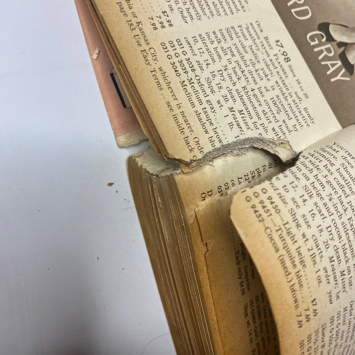 Close-up of the spine of the 1954 Sears Roebuck and Co. Fall and Winter Catalog, showing signs of wear and tear, highlighting its vintage condition.