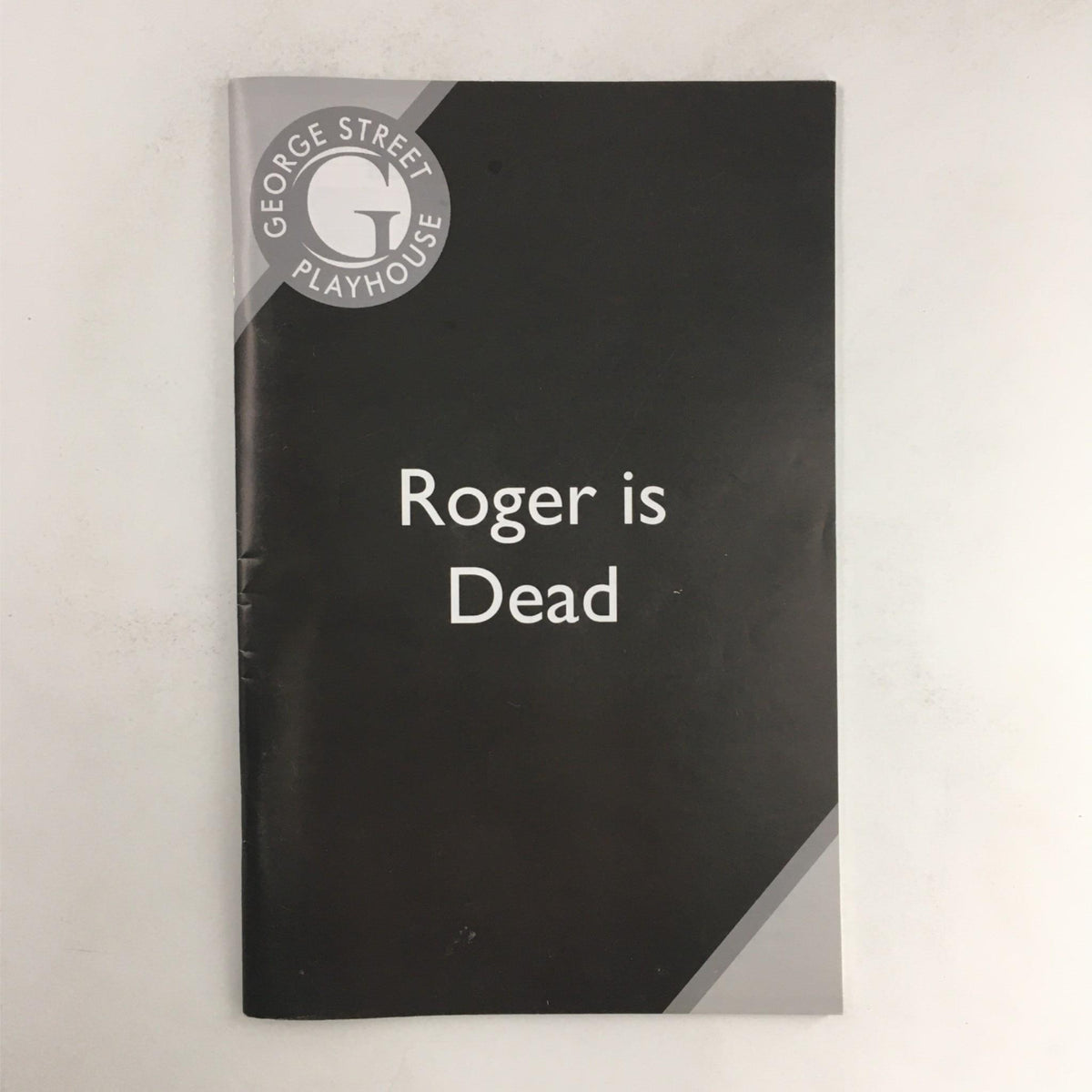 Cover of the play program for 'Roger is Dead' by Elaine May at George Street Playhouse. Features a minimalist black design with the title prominently displayed.