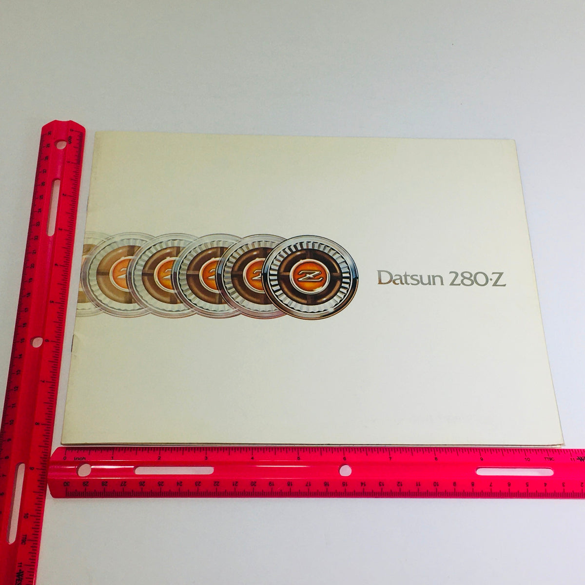 1976 Datsun 280-Z Showroom Specifications Dealership Car Auto Brochure Catalog displayed with a pink ruler for size reference, featuring the iconic Datsun logo and design elements.