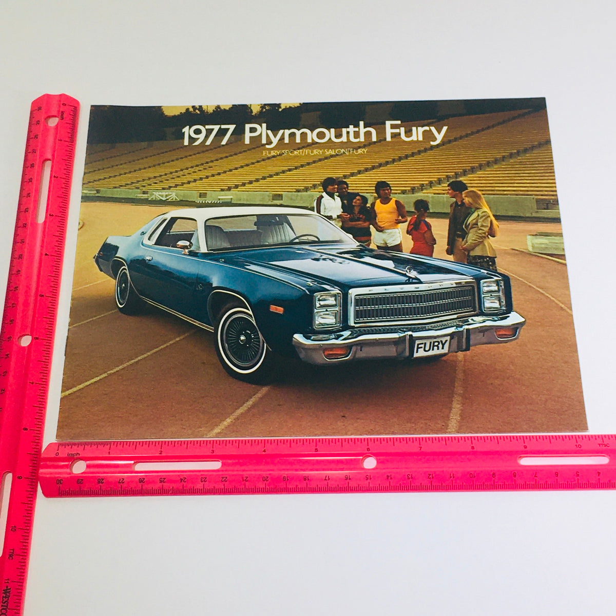 1977 Plymouth Fury Sport-Salon-Fury Dealership Car Auto Brochure Catalog showcasing a blue Plymouth Fury parked on a track with a group of people in the background. The brochure emphasizes 'FURY' with stylish graphics, ideal for car enthusiasts and collectors.