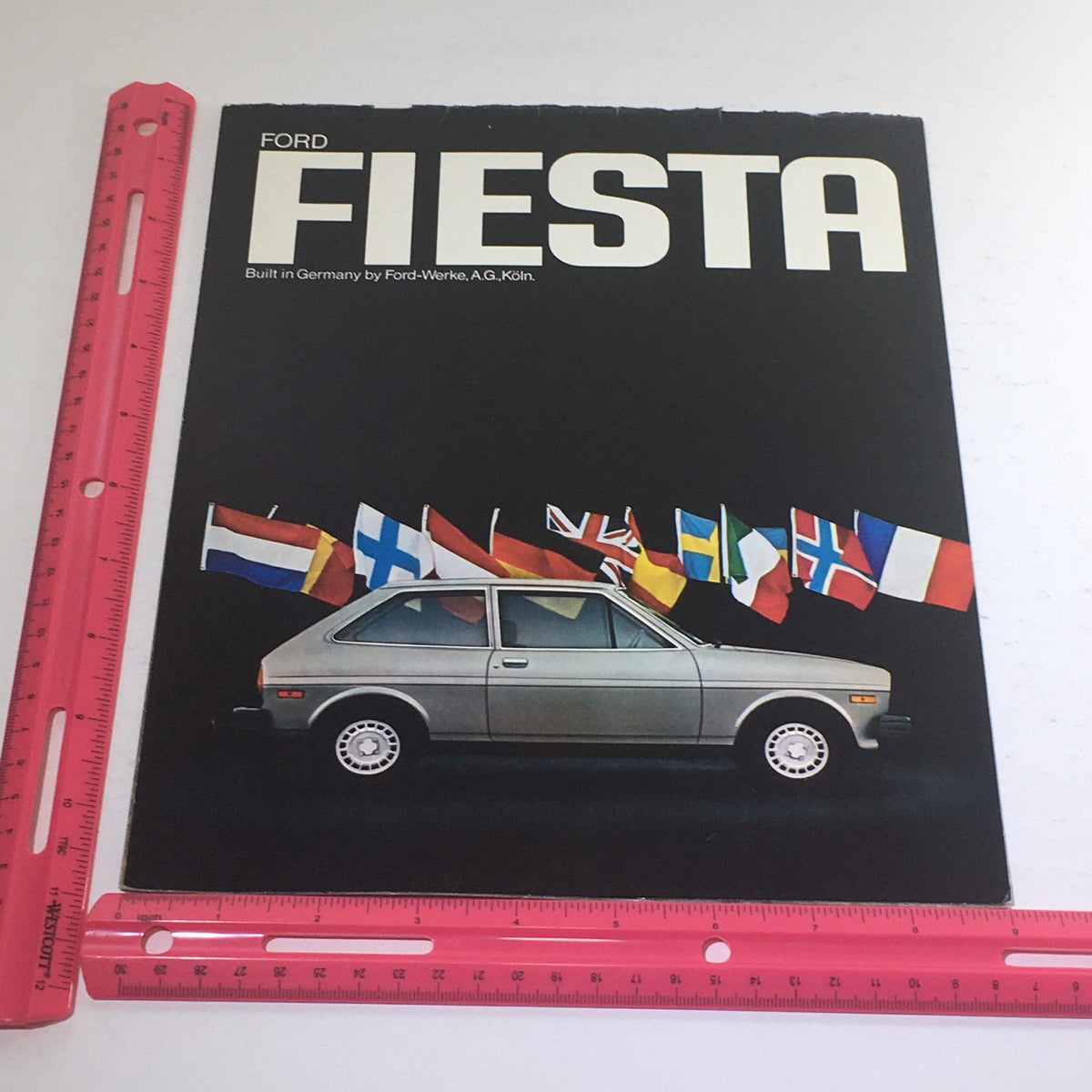 Front cover of the 1976 Ford Fiesta 3-Door Hatchback Dealership Car Auto Brochure Catalog with the car displayed against a backdrop of international flags.