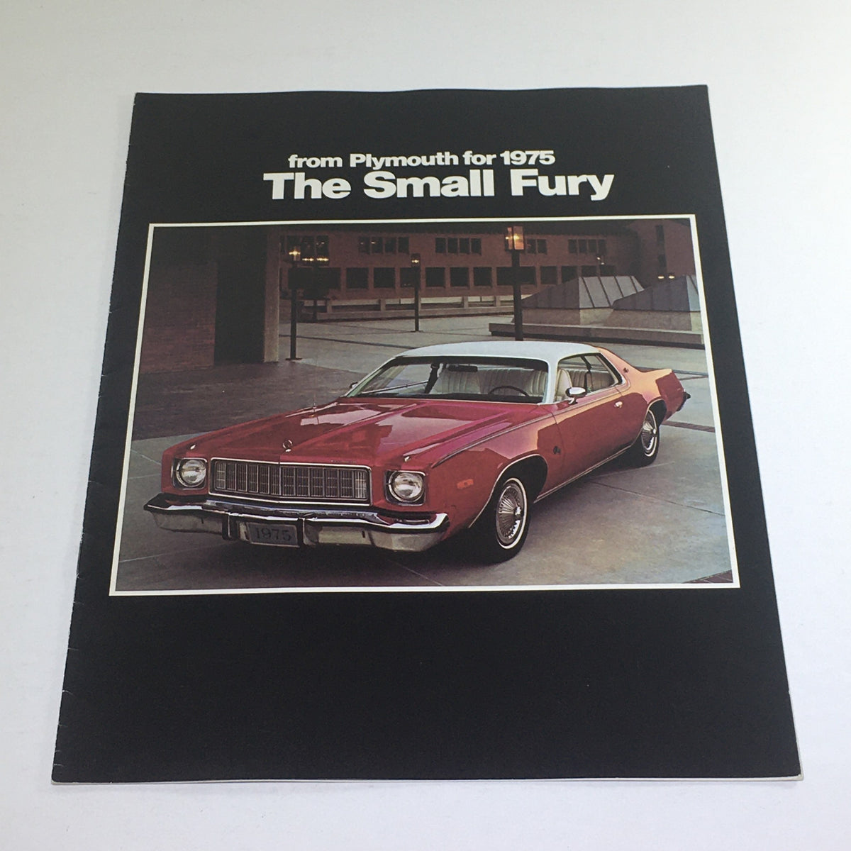 1975 Plymouth Small Fury Custom Sedan dealership car brochure cover featuring a red vehicle parked in an urban setting.