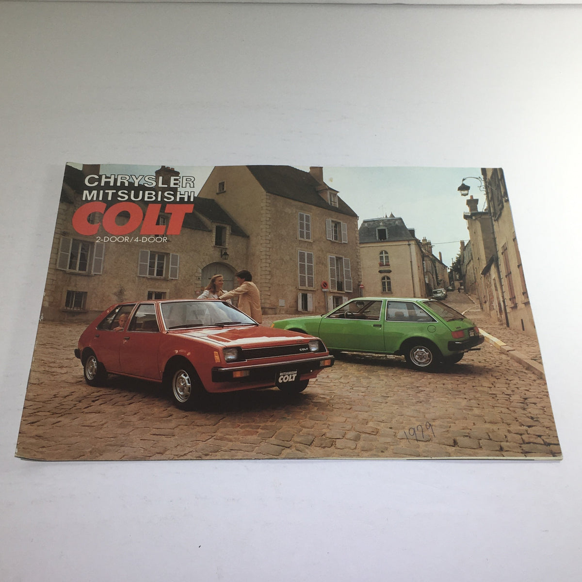 1979 Chrysler-Mitsubishi Colt 2-Door/4-Door Dealership Car Auto Brochure Catalog featuring a red car and a green car parked on cobblestone street with buildings in the background.