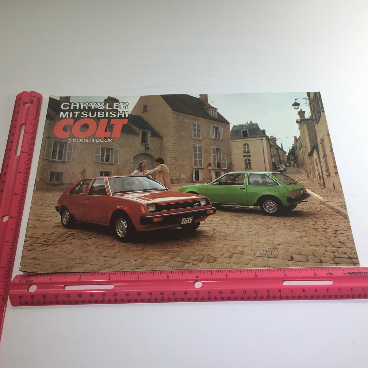 1979 Chrysler-Mitsubishi Colt 2-Door/4-Door Dealership Car Auto Brochure Catalog with an image of a red and green Mitsubishi Colt posed together on a cobblestone street, emphasizing the car's classic design.